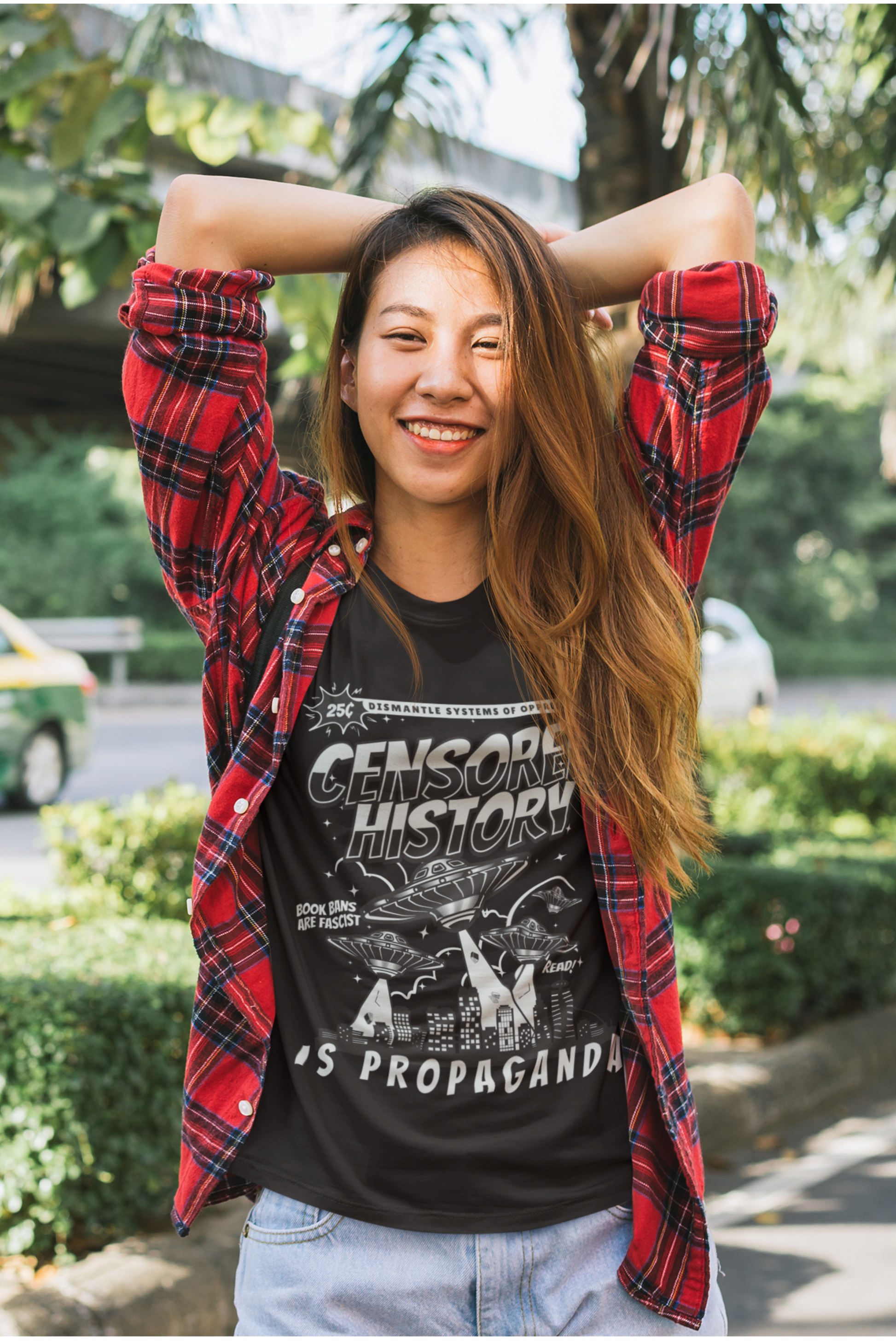 Person wearing a black t-shirt that says Censored History is Propaganda with text and graphics, red plaid shirt, standing outdoors.